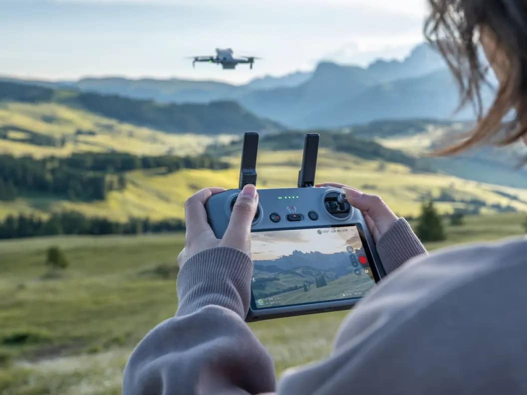 Une pilote de dos suit l’écran de la DJI RC 2, le Mini 5 Pro en vol au loin