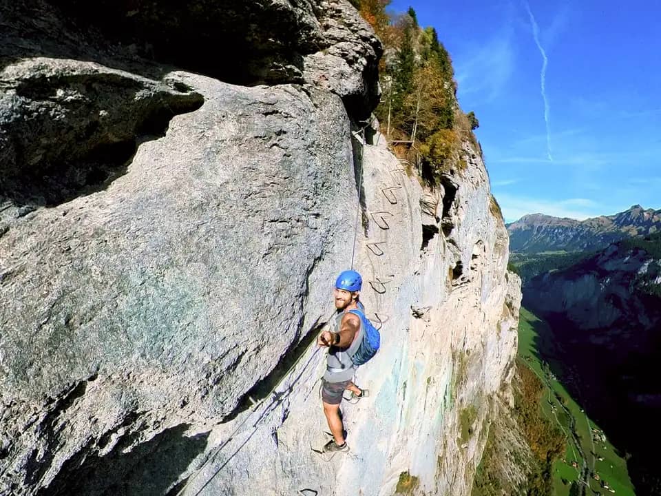 Grimpeur casqué sur une via ferrata, filmé d’en haut au-dessus d’une vallée alpine