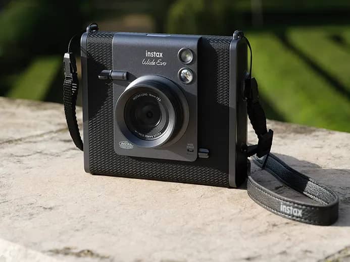 L’instax Wide Evo posé sur un muret de pierre en plein soleil, devant un jardin