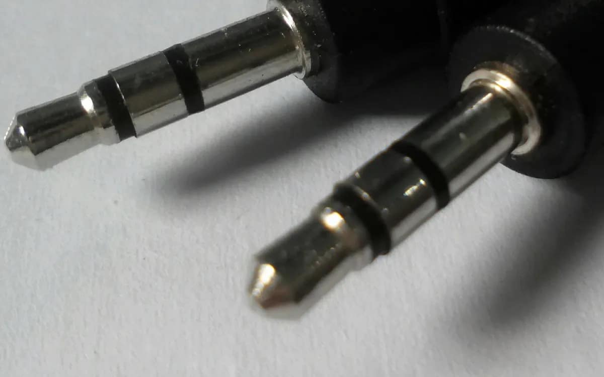 Close-up of two 3.5 mm stereo mini-jack plugs at the ends of their black cables, on a light background