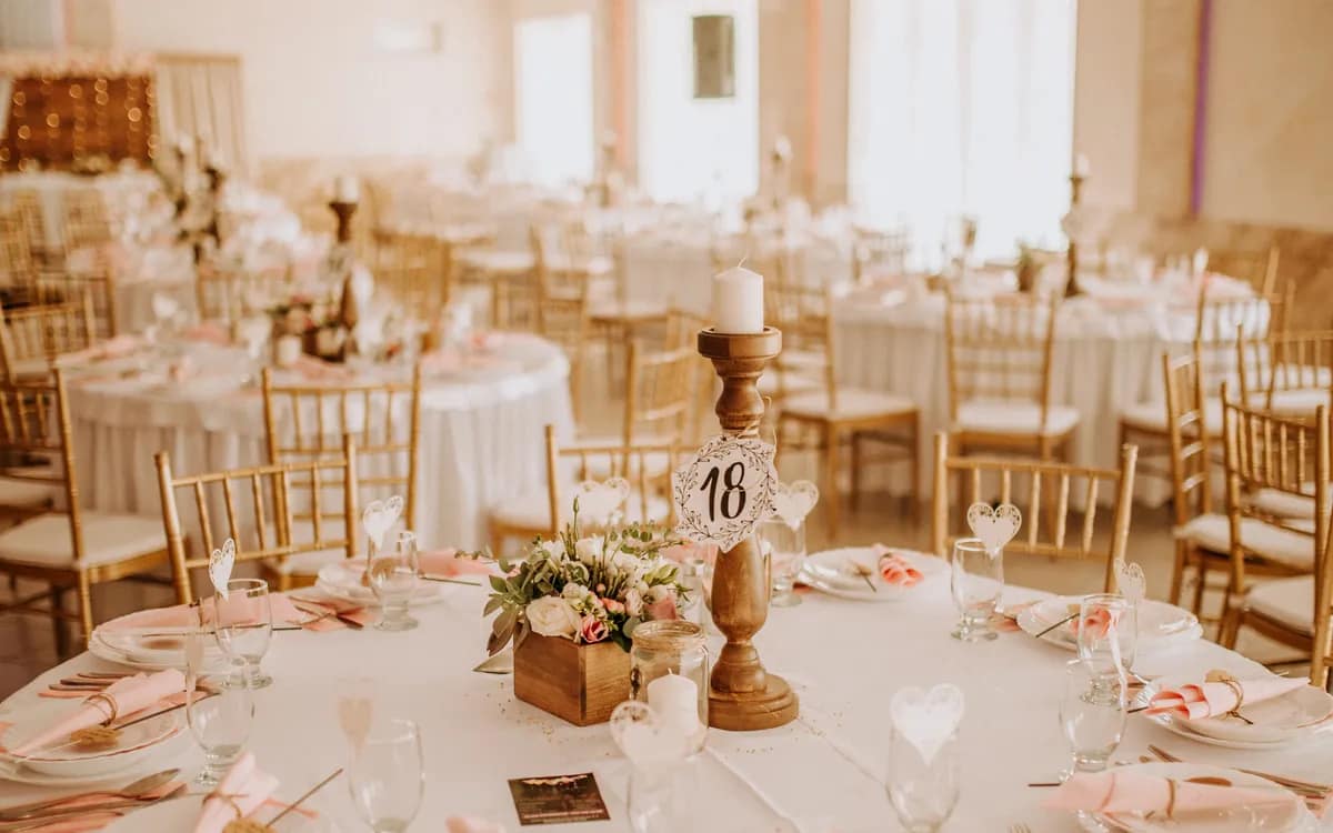 A reception hall set with round tables and gilded chairs, before the guests arrive