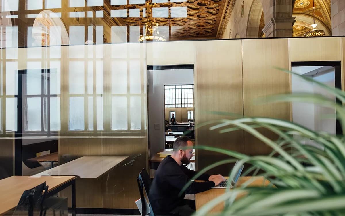 Espace de travail partagé sous une haute verrière, une personne assise devant son ordinateur derrière une cloison vitrée