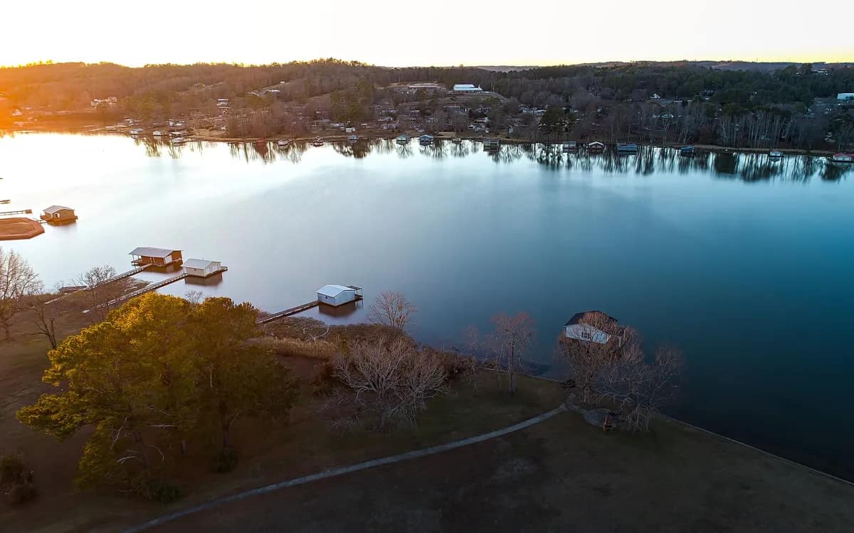 Huizen aan een meer vanuit de lucht, met laagstaande zon die de boomschaduwen over de oever rekt