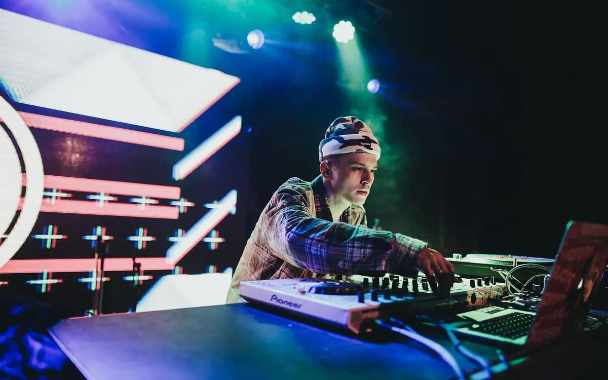 DJ derrière un contrôleur, panneaux lumineux et fumée verte en fond