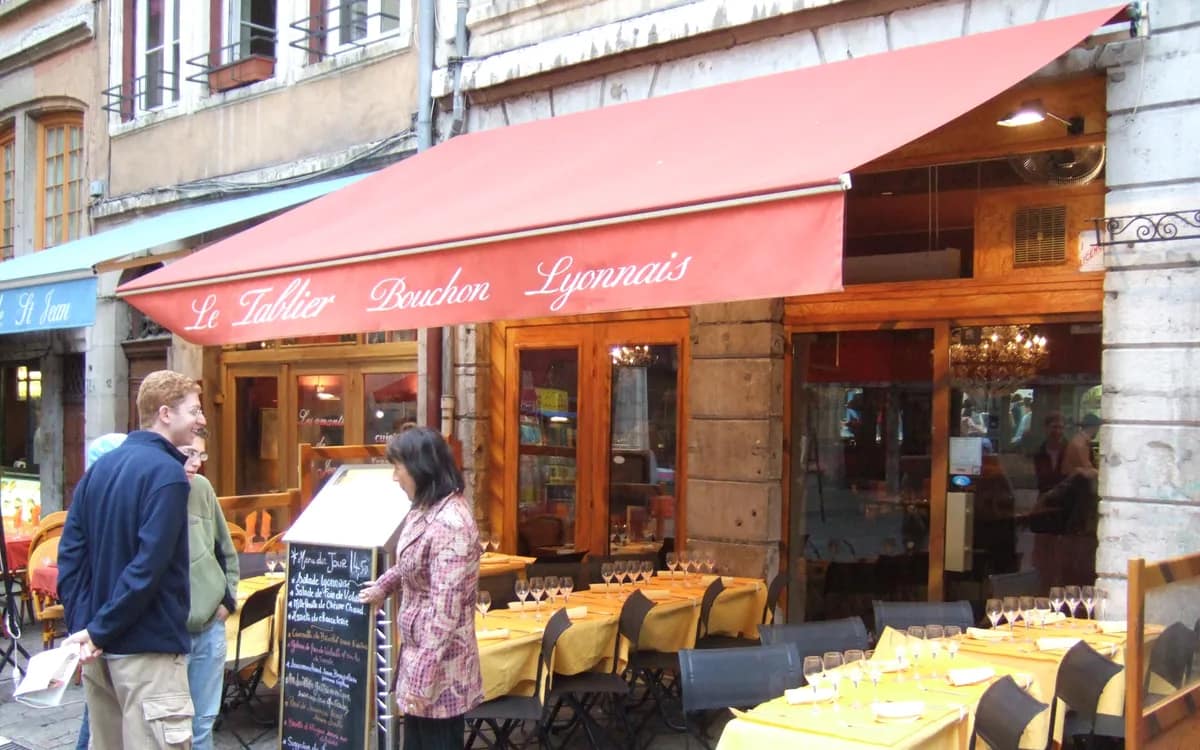 Devanture et terrasse d’un bouchon lyonnais, ardoise du jour posée sur le trottoir