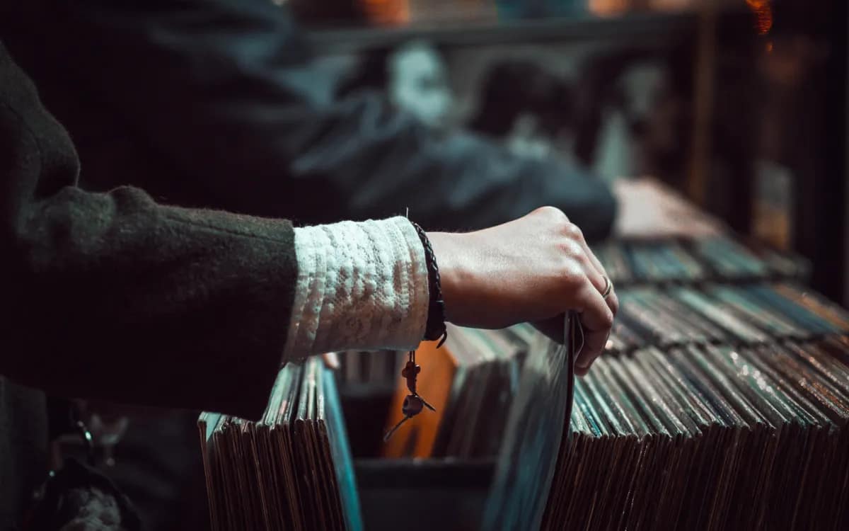 Hands thumbing through a bin of vinyl records in a store, backlit