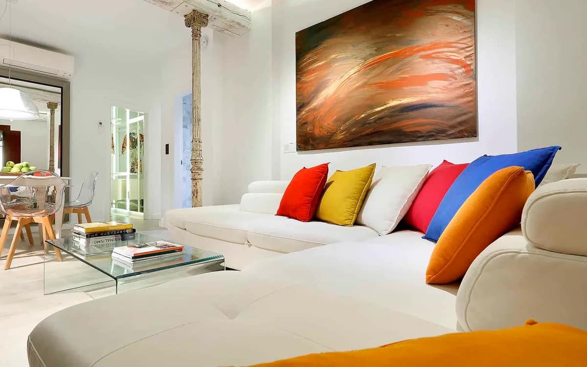 A bright living room in a rental flat, white sofa and colourful cushions