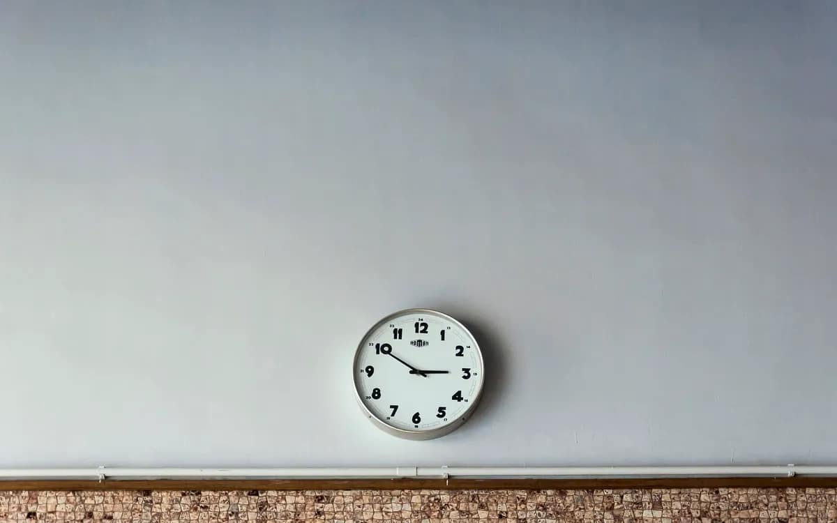 Horloge ronde à cadran blanc accrochée seule sur un grand mur clair