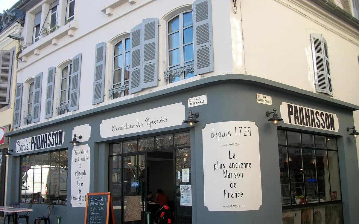 The frontage of an old chocolate shop on a street corner, grey-blue façade