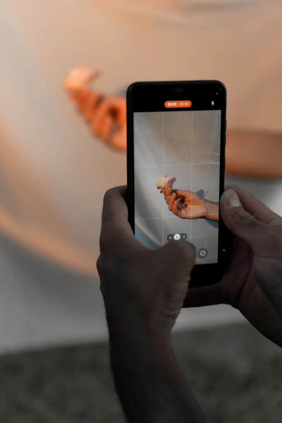 Deux mains filment une fleur à la verticale avec un smartphone