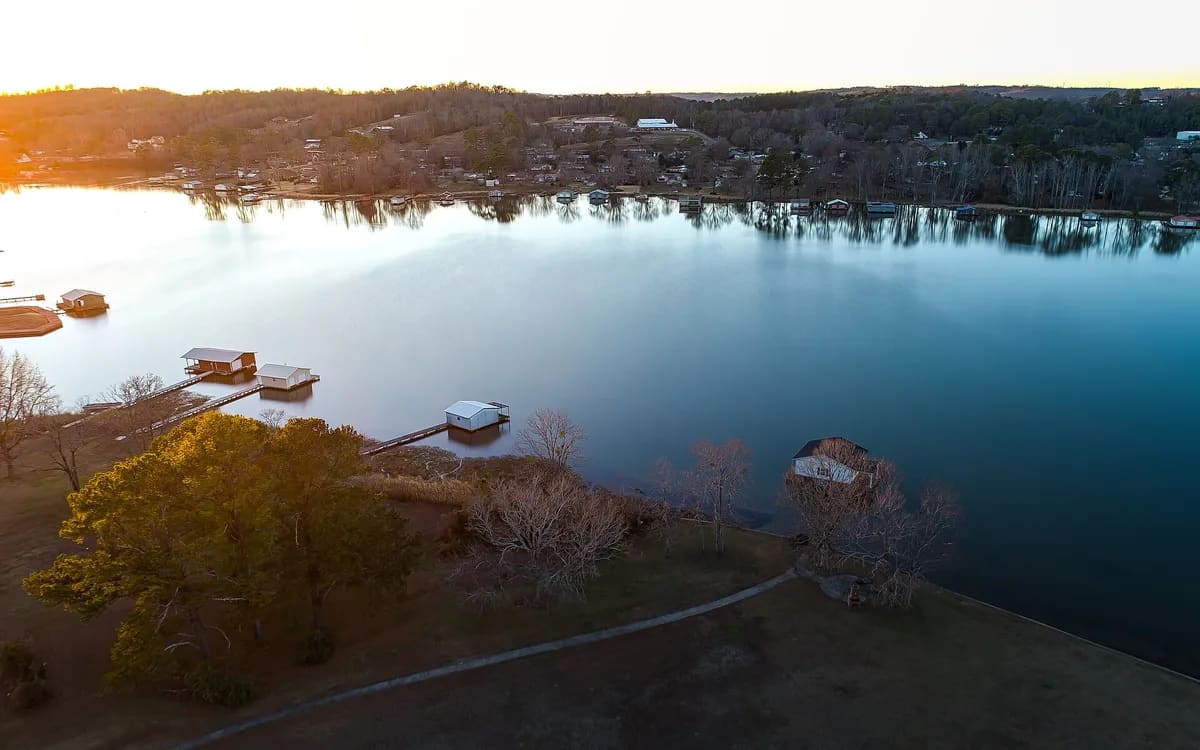 Huizen aan een meer vanuit de lucht, met laagstaande zon die de boomschaduwen over de oever rekt