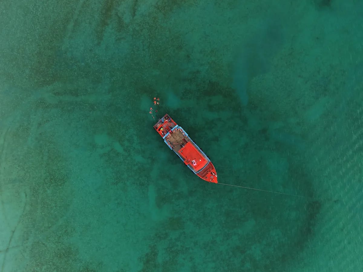Vue aérienne à la verticale d’une barque en bois amarrée sur une eau turquoise très claire