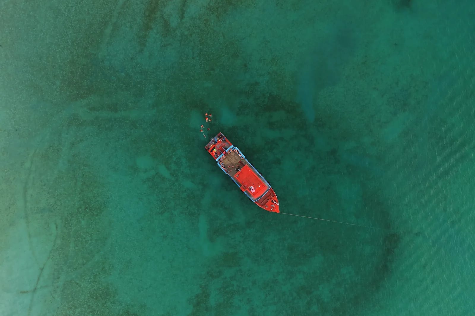 Overhead aerial view of a wooden boat moored on very clear turquoise water