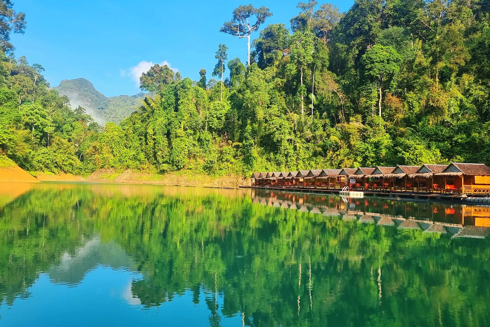 Calm lake fringed by dense tropical forest, with wooden floating huts mirrored in the water