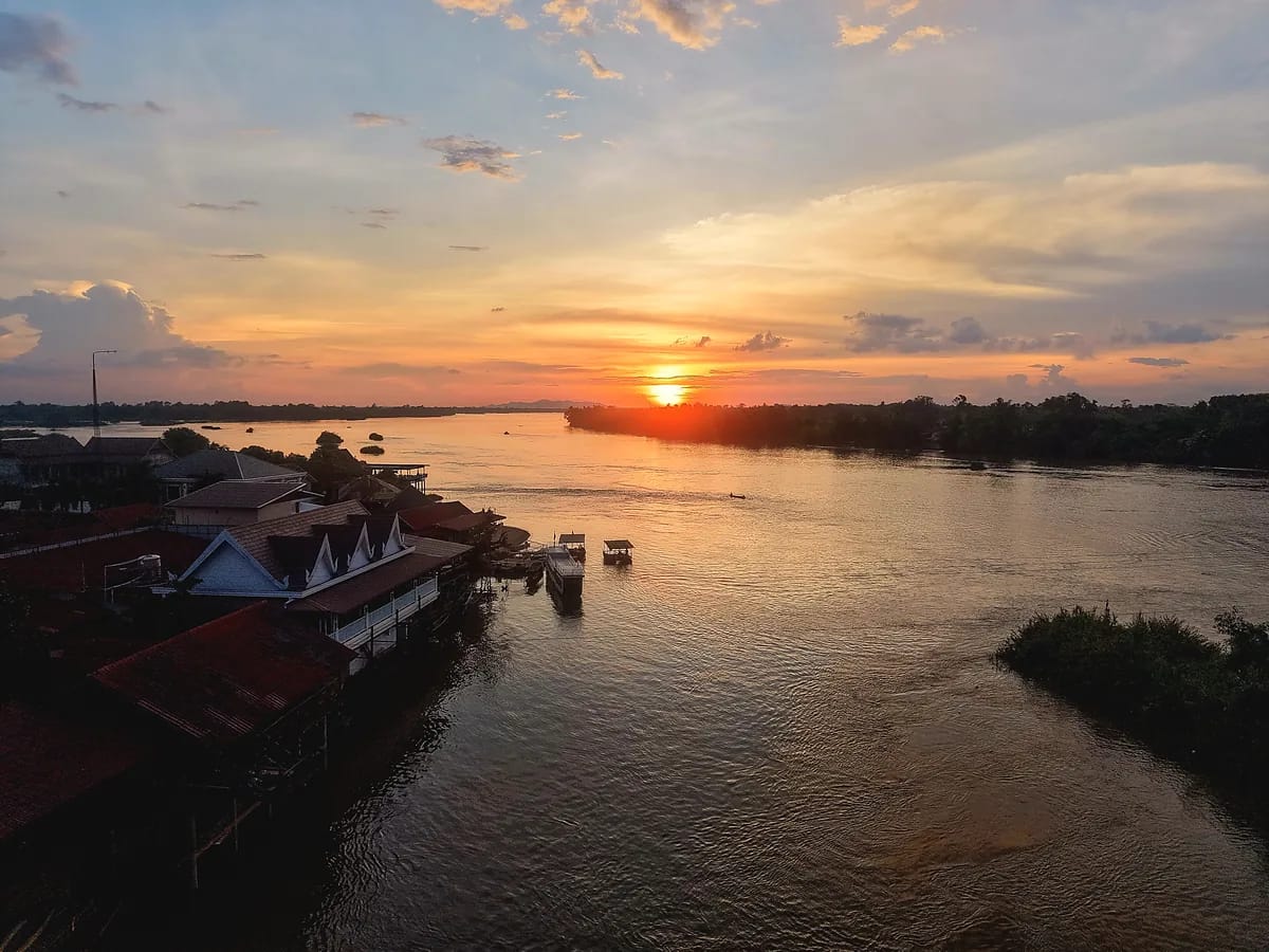 Coucher de soleil vu du ciel sur un large fleuve bordé de maisons sur pilotis