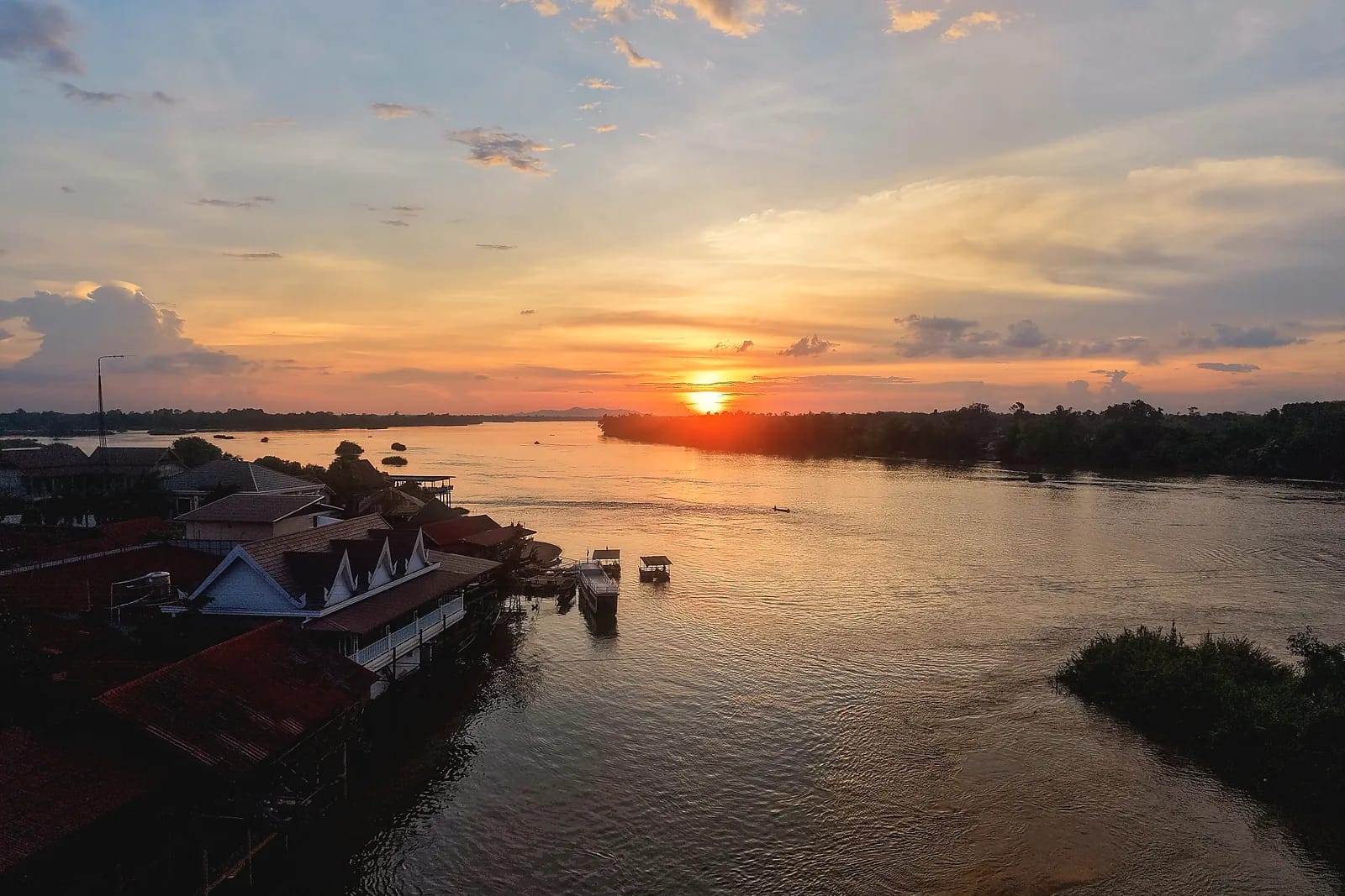 Sunset seen from the air over a wide river lined with stilt houses