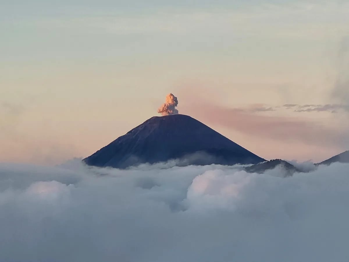 Sommet d’un volcan émergeant d’une mer de nuages au lever du jour, avec un panache de fumée