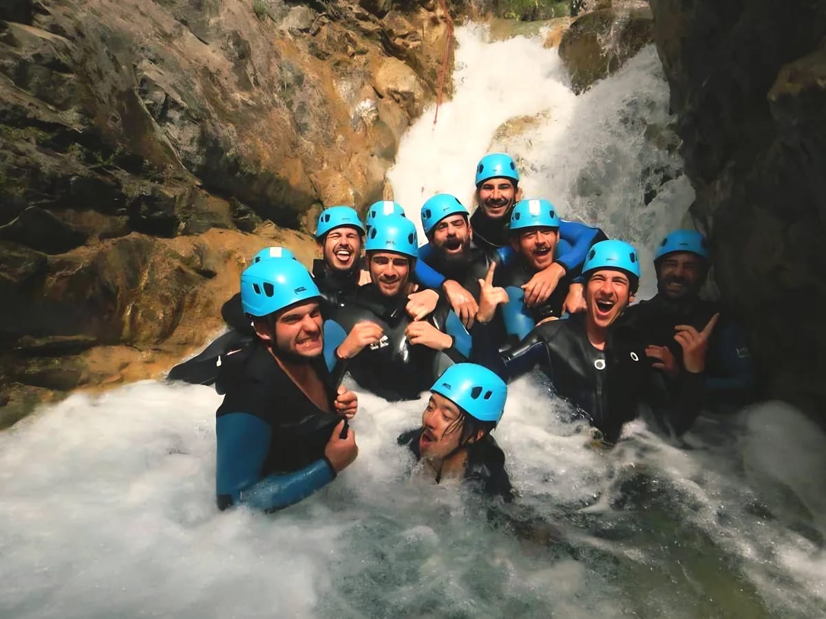 Groupe de canyonistes en combinaison et casque dans l’eau vive au pied d’une cascade