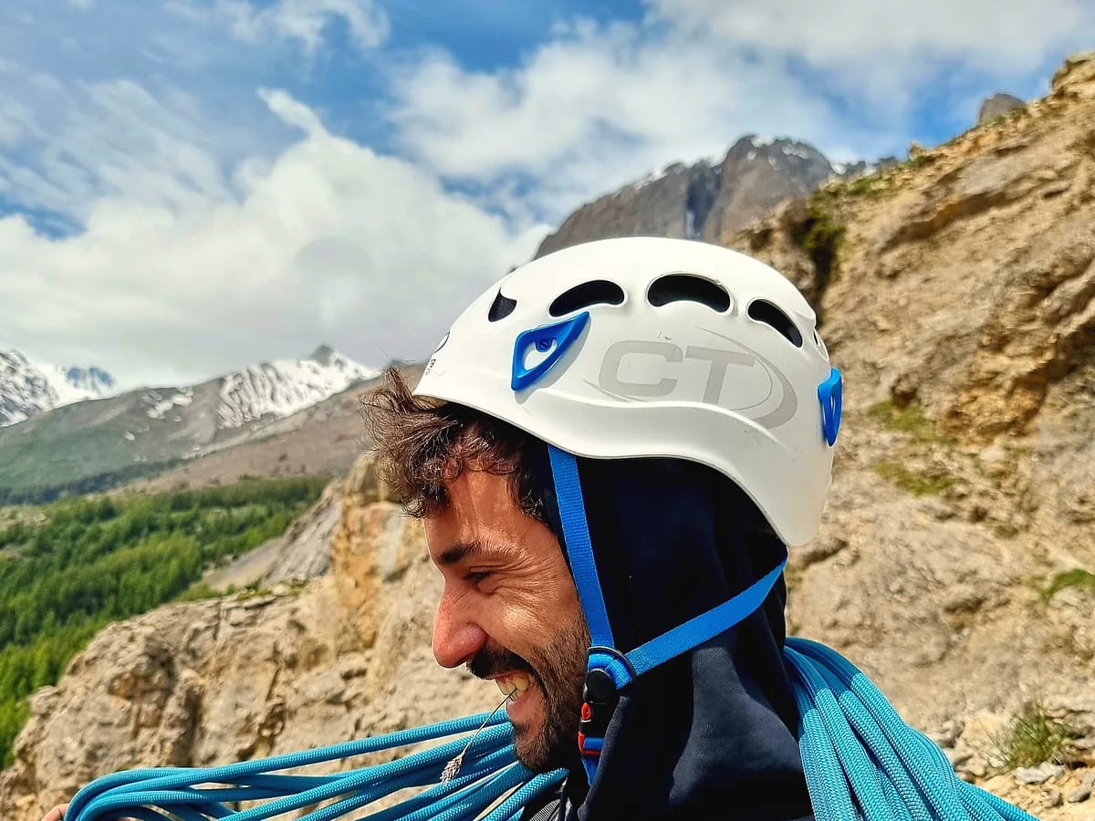 Grimpeur casqué lovant une corde d’escalade, massif rocheux et cimes enneigées en arrière-plan