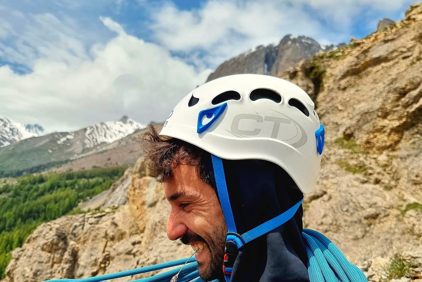 Grimpeur casqué lovant une corde d’escalade, massif rocheux et cimes enneigées en arrière-plan