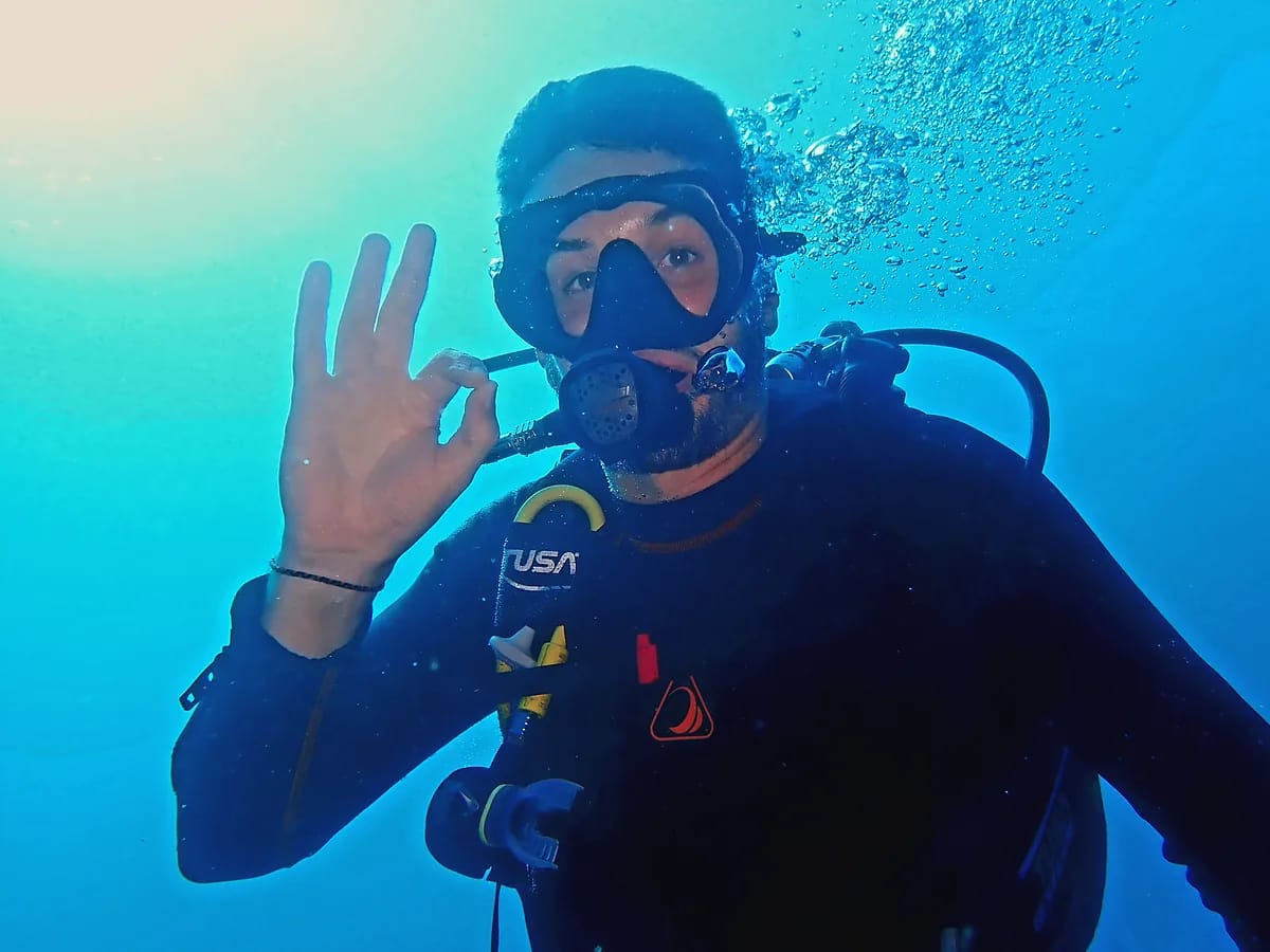 Plongeur en scaphandre faisant le signe OK sous l’eau, dans une mer bleue traversée de lumière