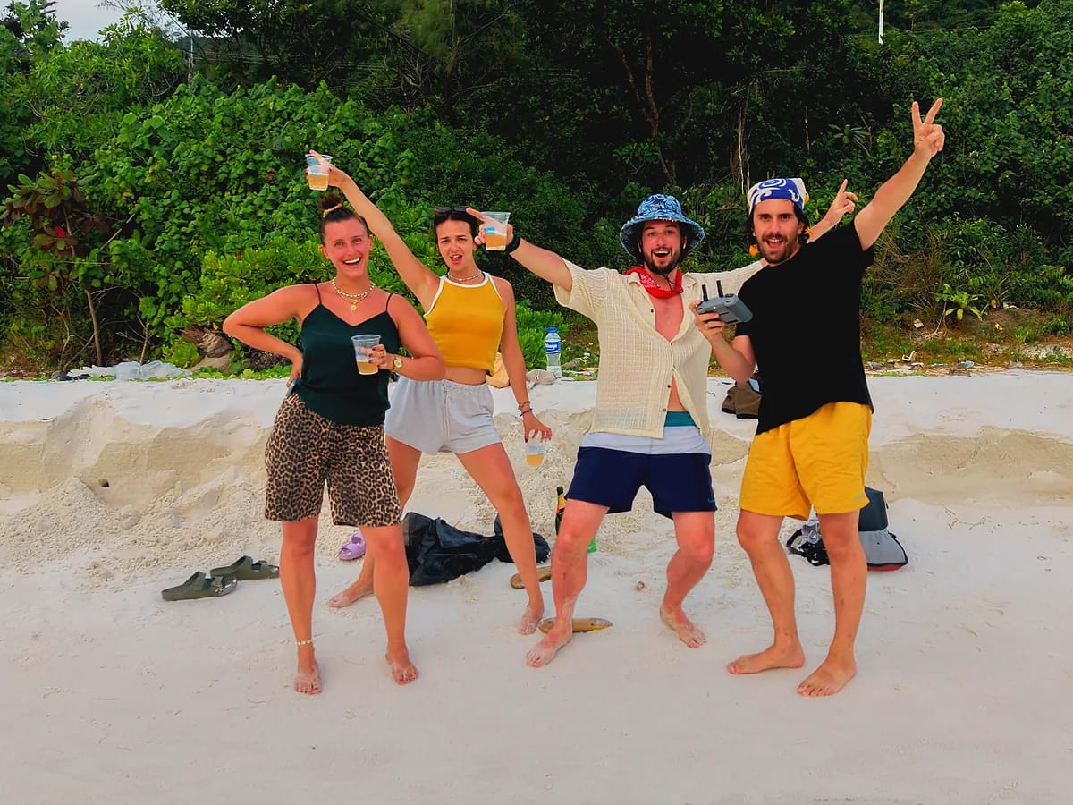 Quatre amis posant sur une plage de sable blanc, l’un tenant une radiocommande de drone