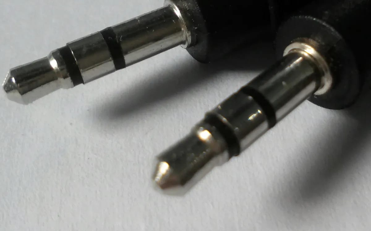 Close-up of two 3.5 mm stereo mini-jack plugs at the ends of their black cables, on a light background