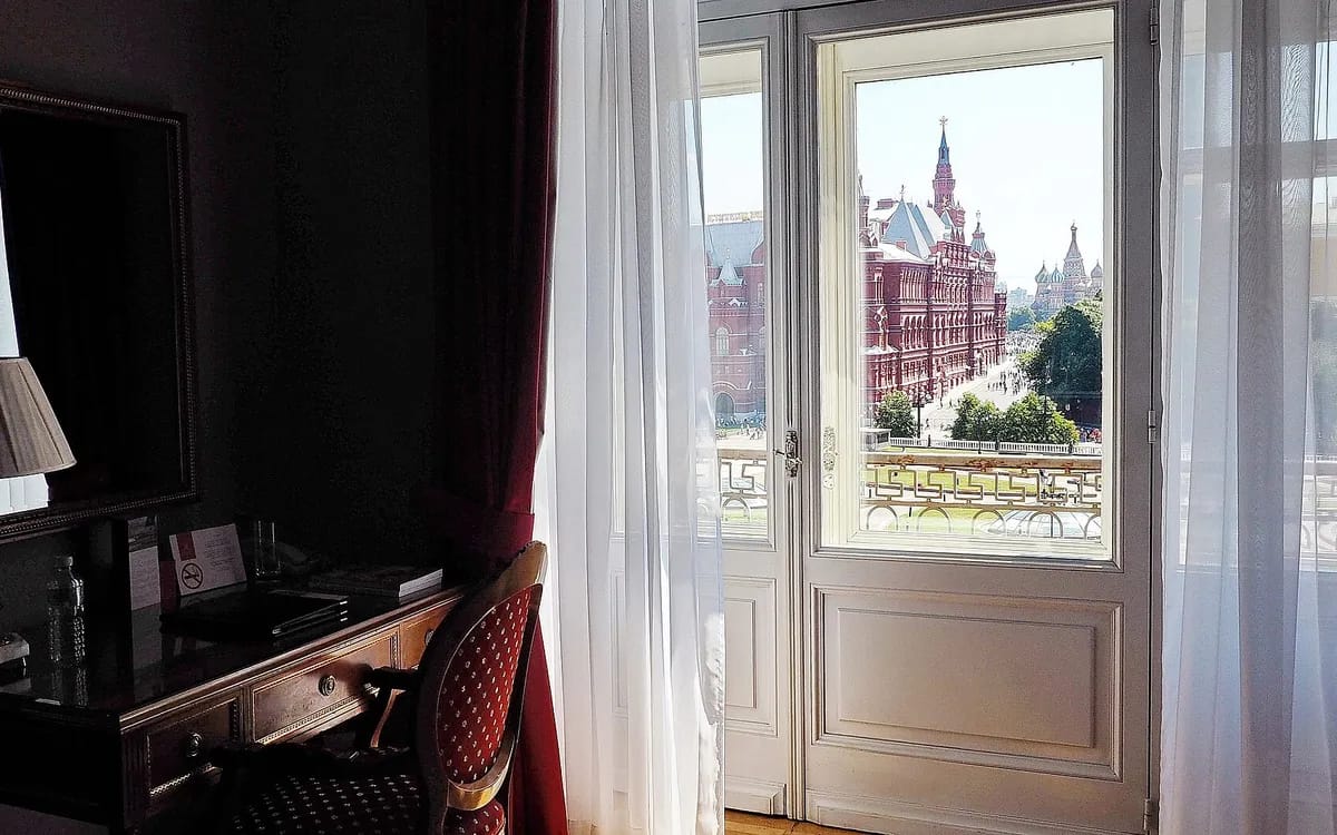 Chambre d’hôtel sombre ouverte sur une porte-fenêtre et une place ensoleillée