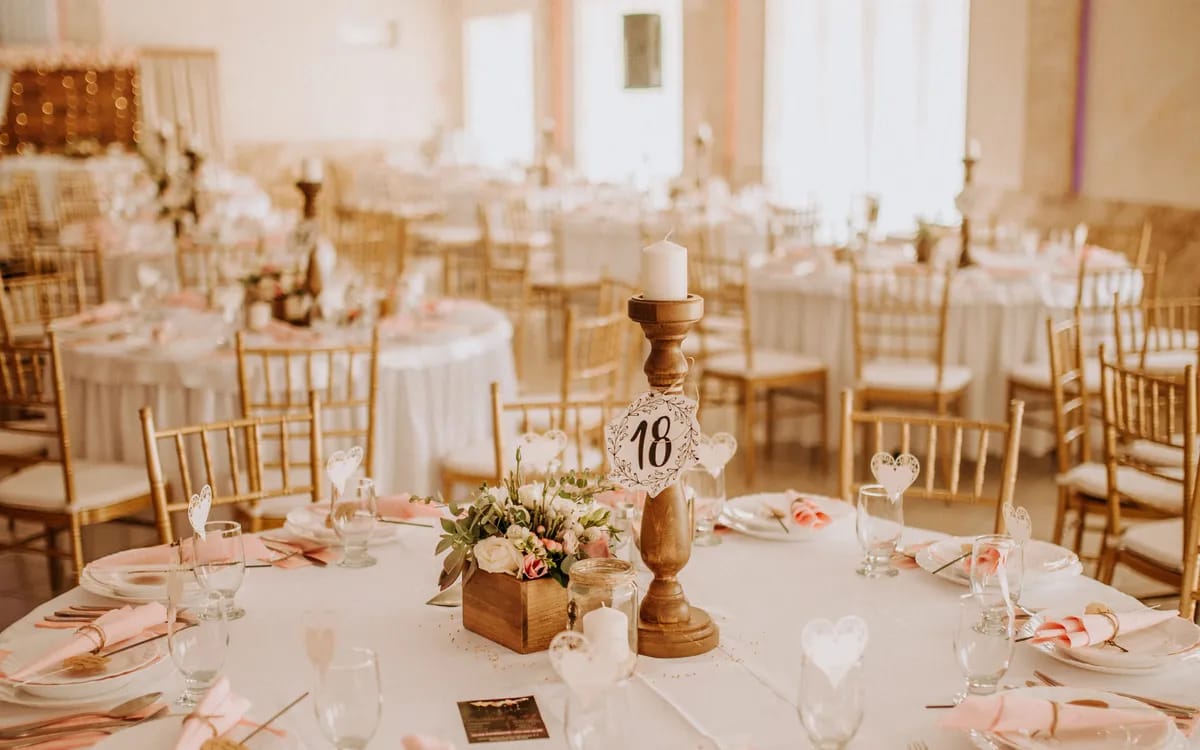 A reception hall set with round tables and gilded chairs, before the guests arrive