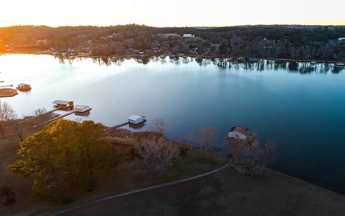 Huizen aan een meer vanuit de lucht, met laagstaande zon die de boomschaduwen over de oever rekt