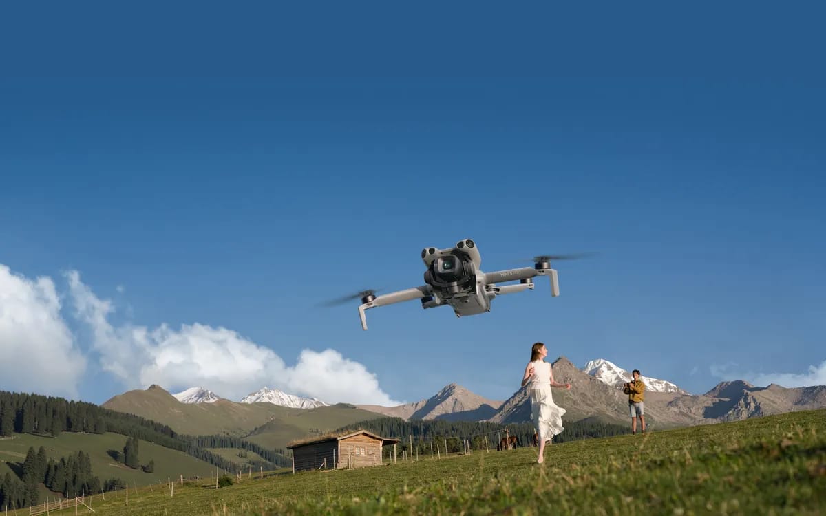 Drone DJI Mini 5 Pro en vol au-dessus d’un alpage, montagnes enneigées à l’arrière-plan