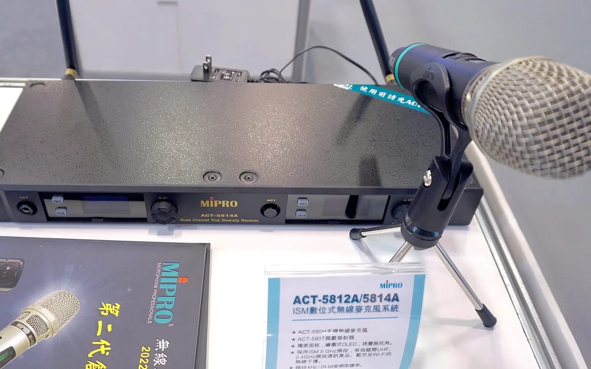 Récepteur de micro sans fil quatre canaux posé sur une table, ses deux antennes dressées, et un micro main HF sur un petit pied à côté.