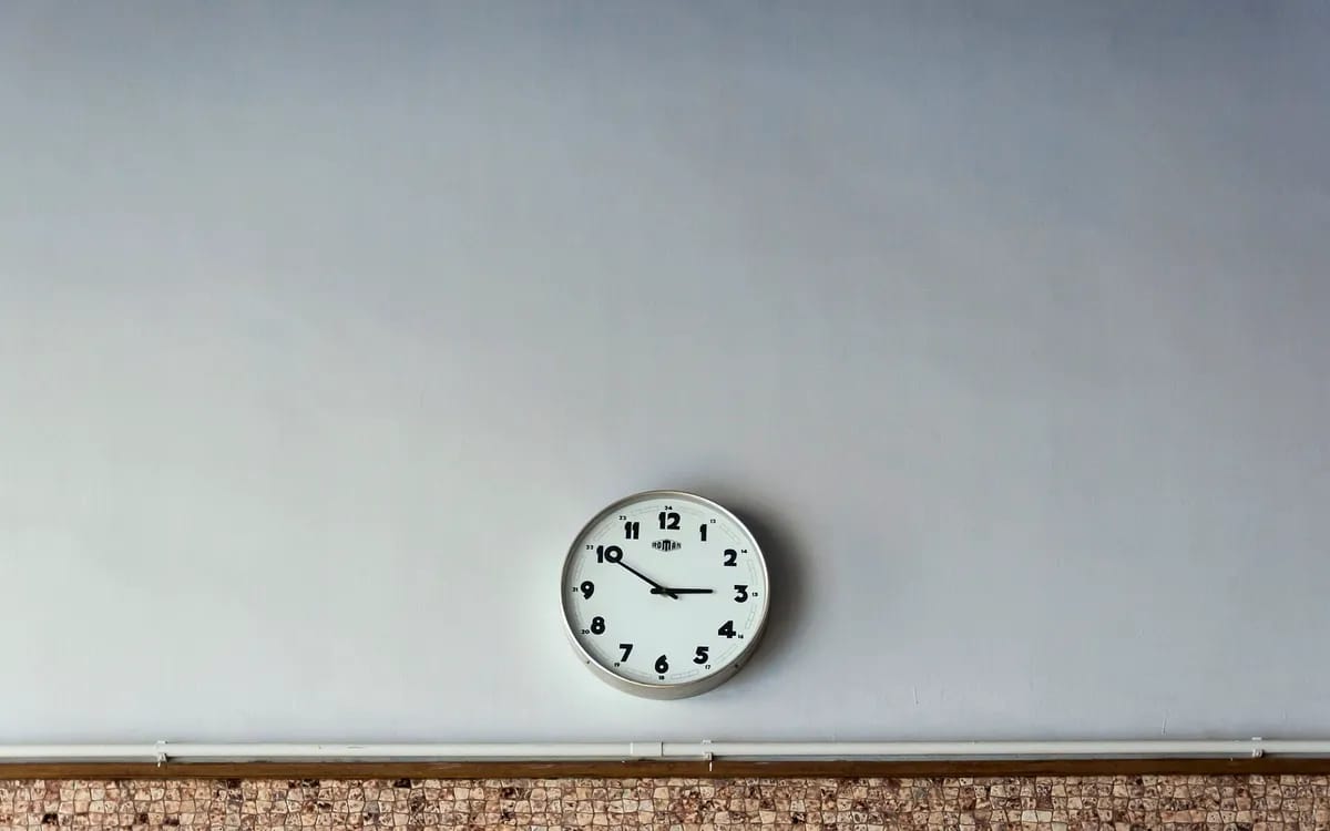 Runde Uhr mit weißem Zifferblatt, allein an einer großen hellen Wand