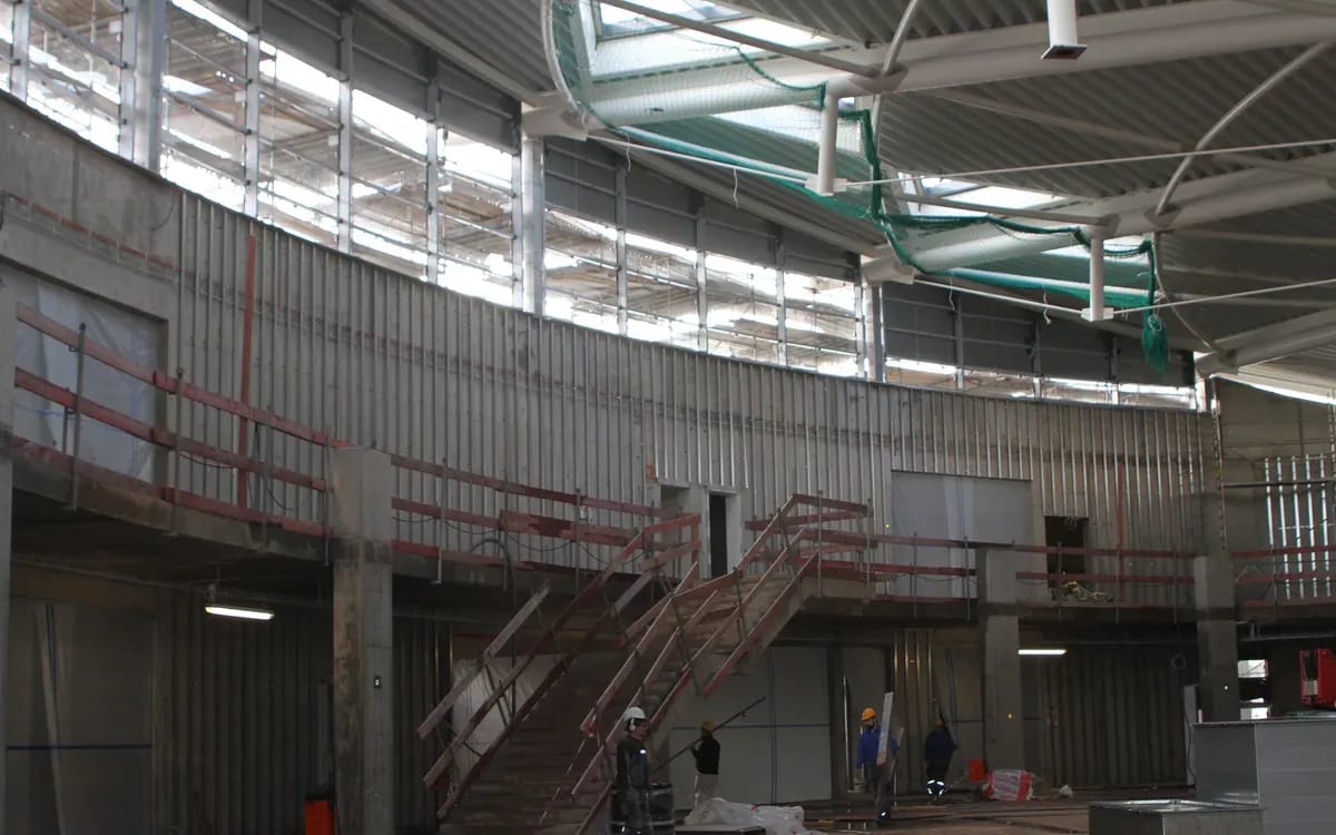 Intérieur d’un bâtiment en construction : sol brut, escalier métallique et grandes verrières