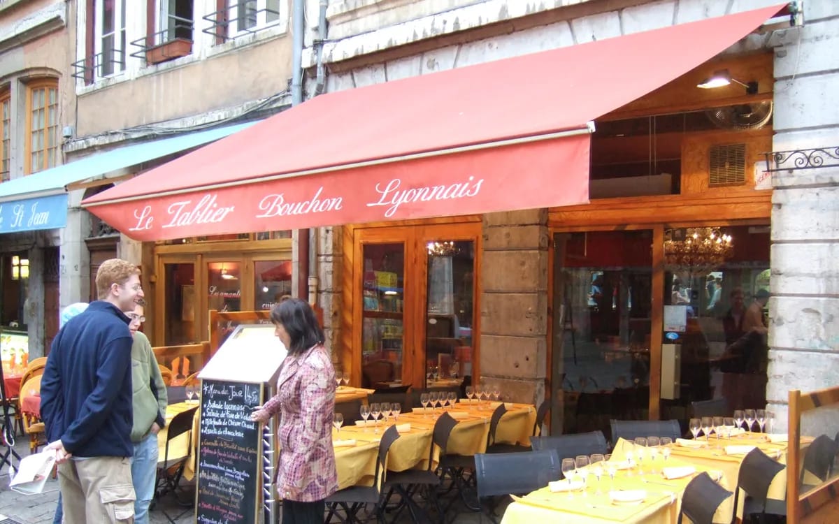 Devanture et terrasse d’un bouchon lyonnais, ardoise du jour posée sur le trottoir