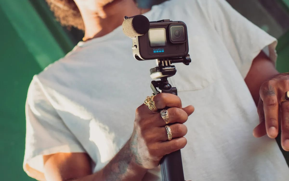 GoPro HERO équipée du module médias et d’un micro externe, tenue à la main sur une poignée
