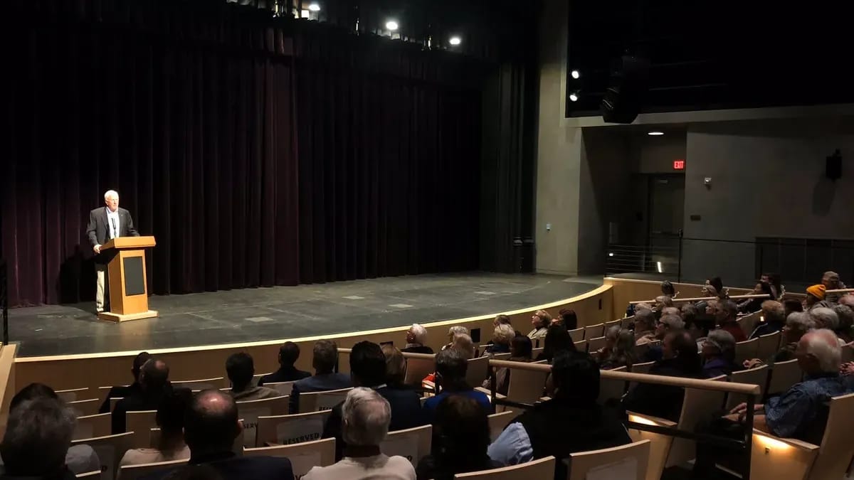 Un orateur au pupitre sur la scène d’un auditorium, devant le public