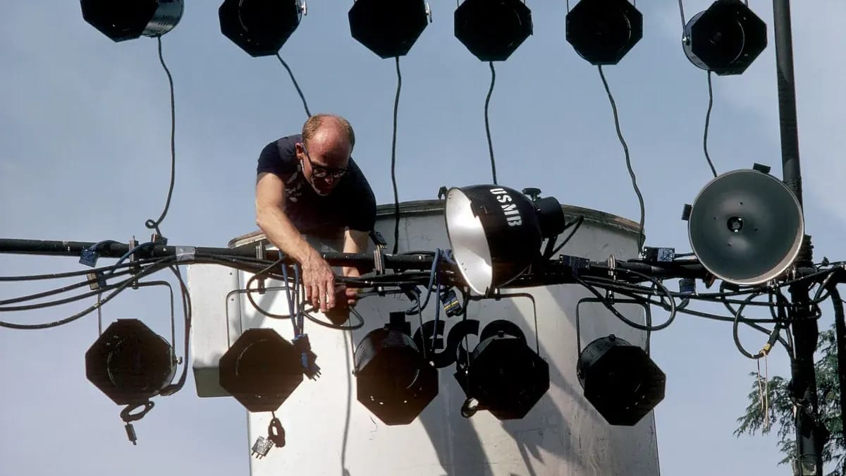 Un technicien accroche des projecteurs sur une structure, vu d’en bas