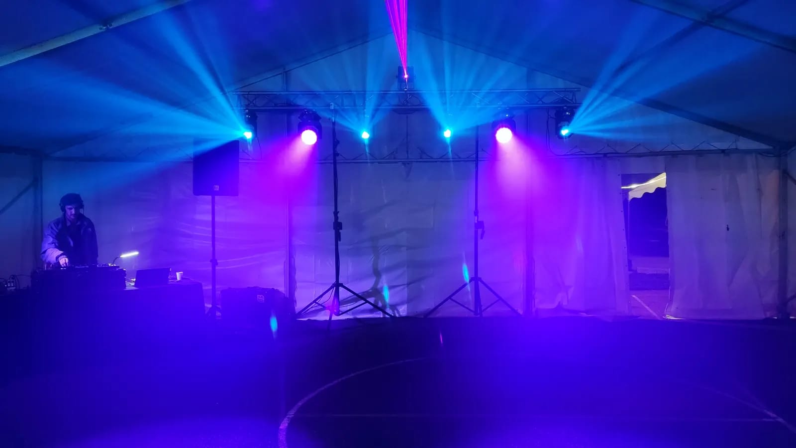 Chapiteau blanc plongé dans la brume : faisceaux bleus et violets au-dessus d’une piste de danse, un DJ à sa régie