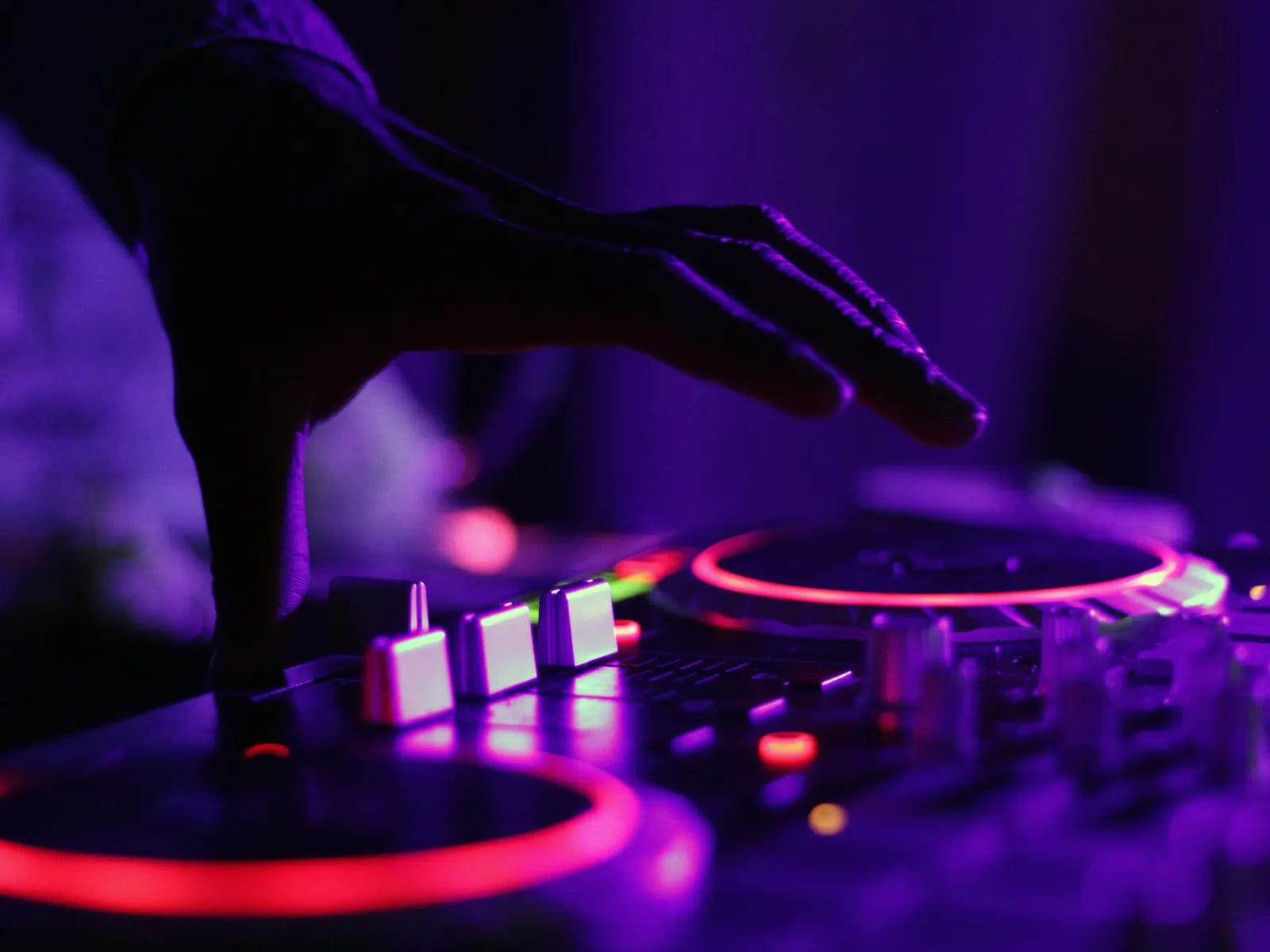 Main d’un DJ au-dessus d’une console éclairée de rouge et de violet