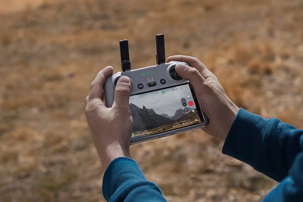Pilote tenant à deux mains une radiocommande DJI RC 2 à écran intégré, en extérieur