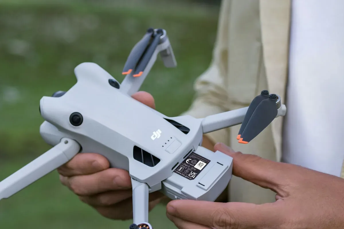 Mains insérant une batterie dans un petit drone gris DJI, en extérieur