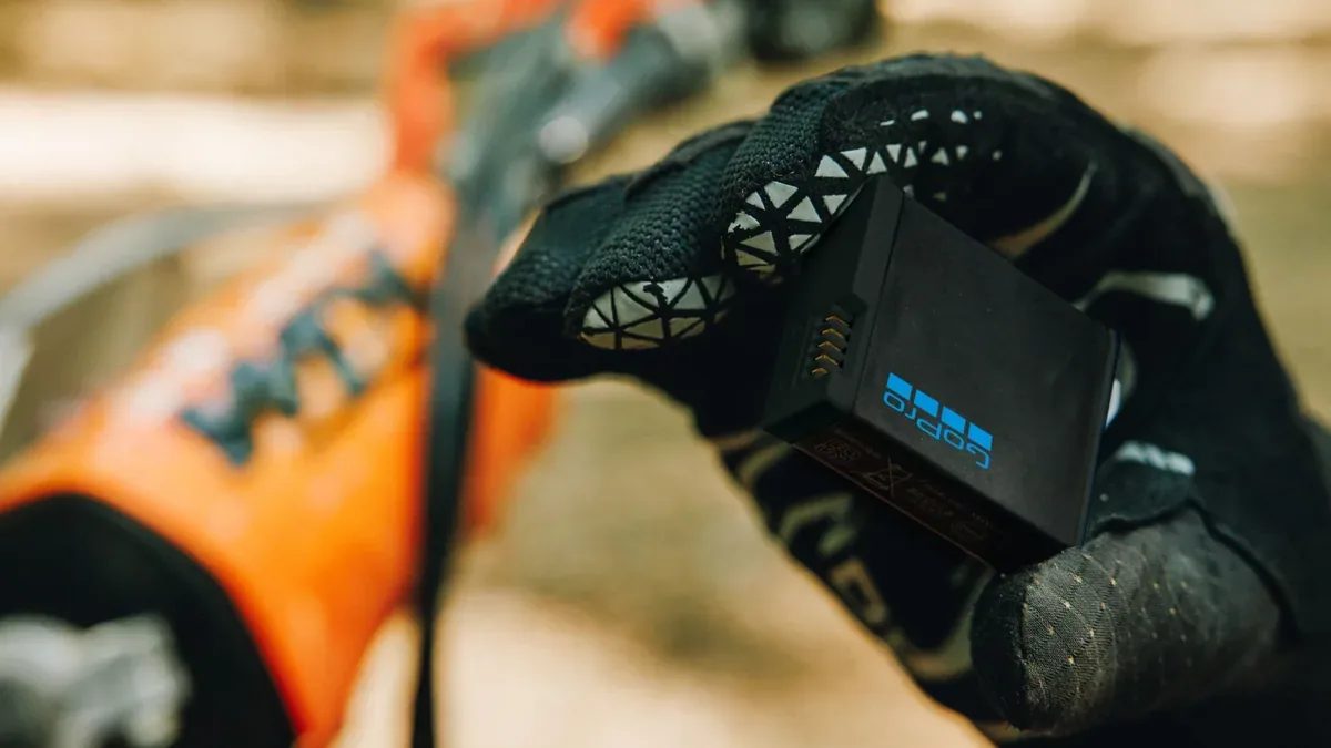 Main gantée tenant une batterie GoPro Enduro noire, en extérieur