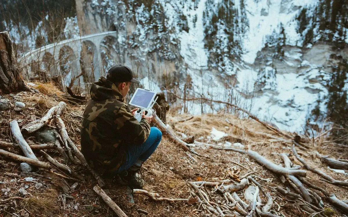 Télépilote accroupi dans un paysage enneigé, radiocommande à écran entre les mains