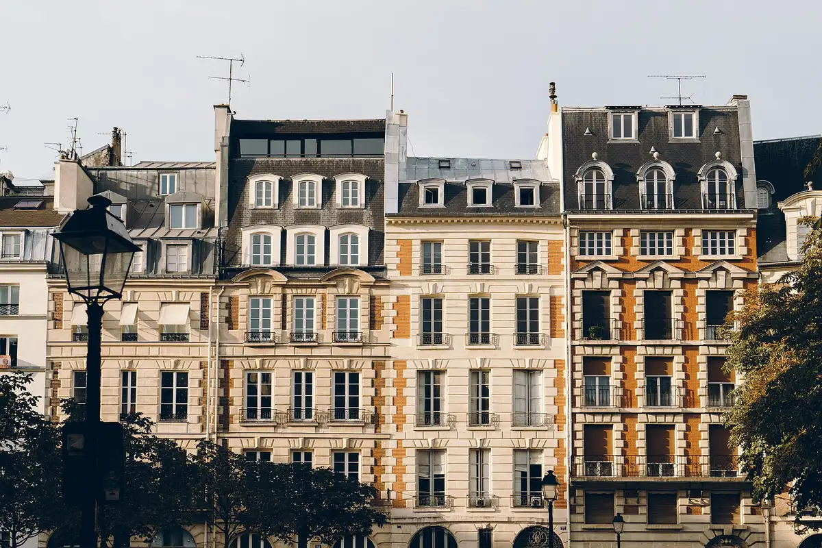 Façades haussmanniennes alignées sur une place parisienne, arbres et réverbère