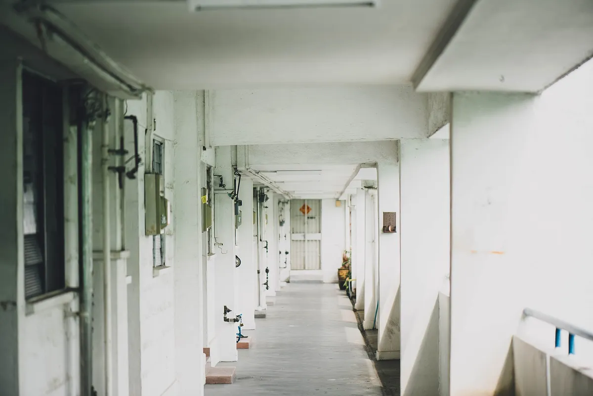 Coursive extérieure d’immeuble, portes alignées et sol de béton nu