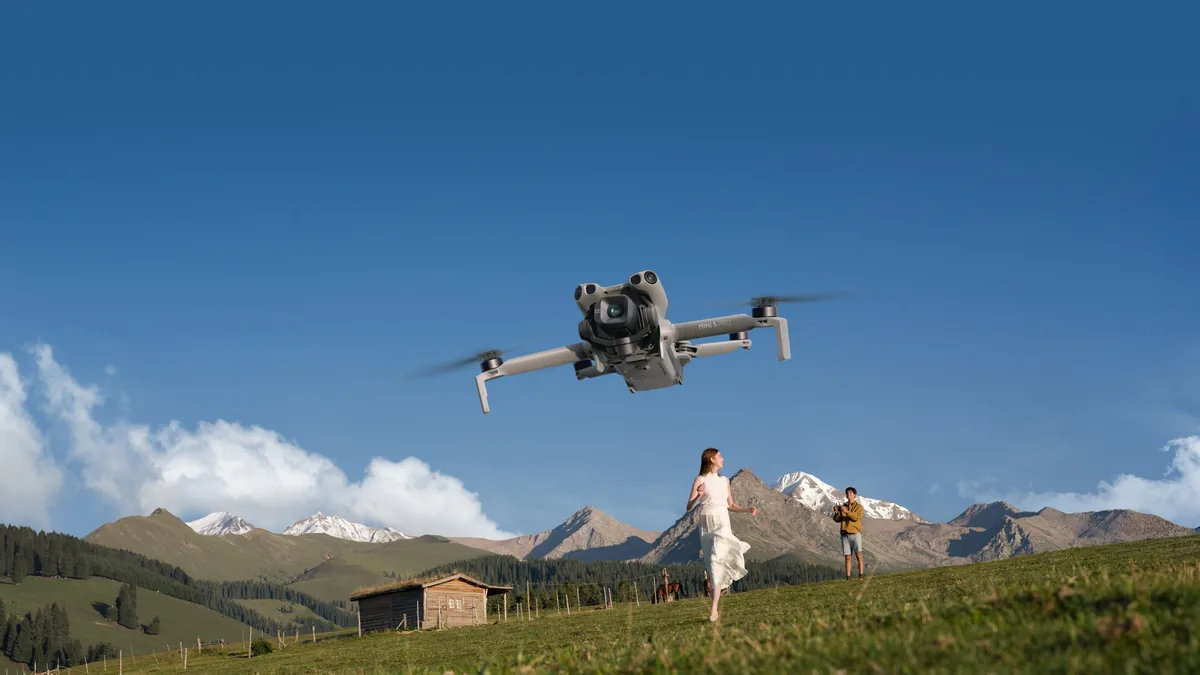 Drone DJI Mini 5 Pro en vol au-dessus d’un alpage, sommets enneigés à l’arrière-plan