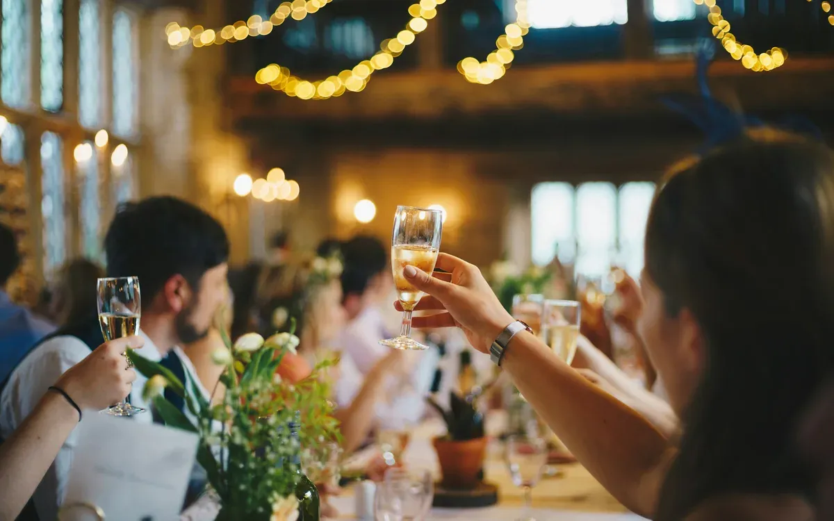 Convives attablés levant leurs verres sous des guirlandes lumineuses, dans une salle chaleureuse