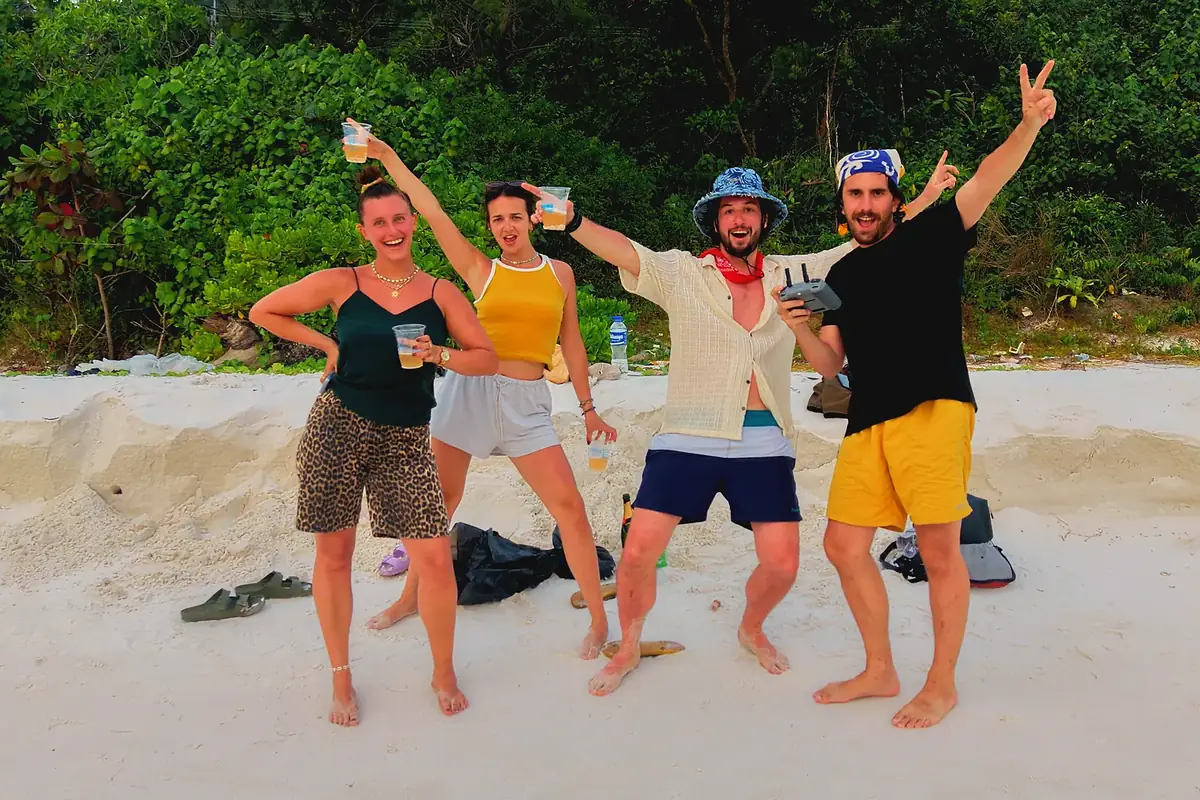 Quatre amis posant sur une plage de sable blanc, l'un tenant une radiocommande de drone
