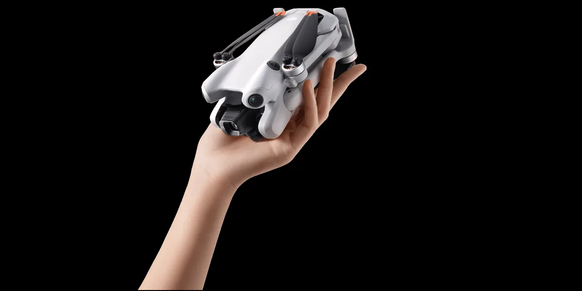 Main tenant un drone DJI Mini replié, qui tient dans la paume, sur fond noir
